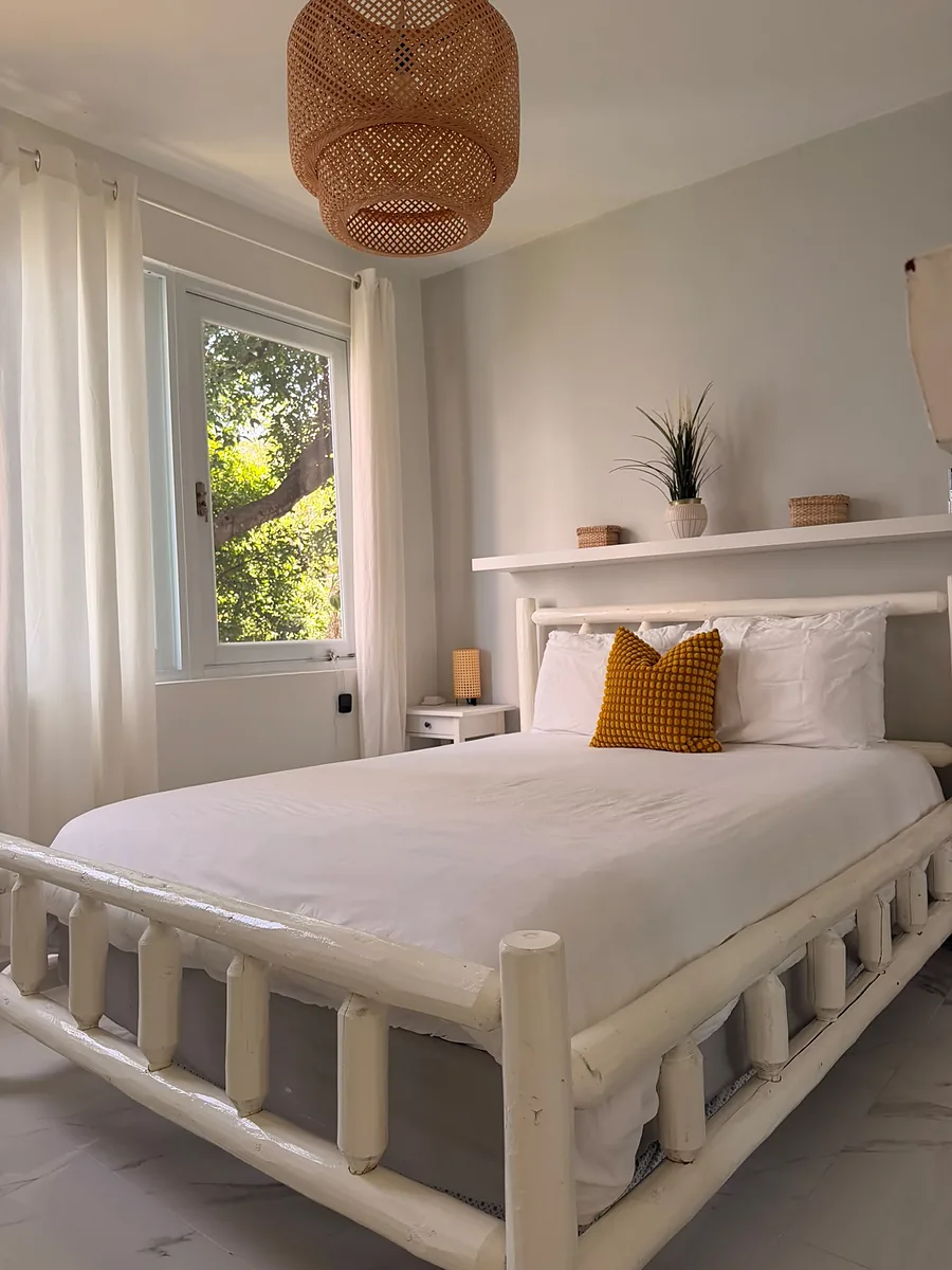 Habitación de un Airbnb con la cama tendida en blanco, cabecera de madera clara y luz natural, lista para el próximo huésped