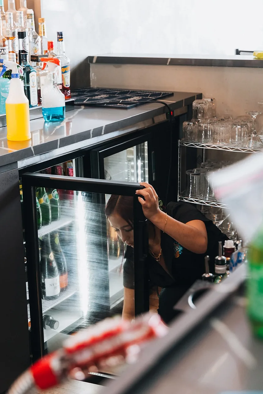 Empleada de Clean Vibes organizando la nevera de botellas de una barra